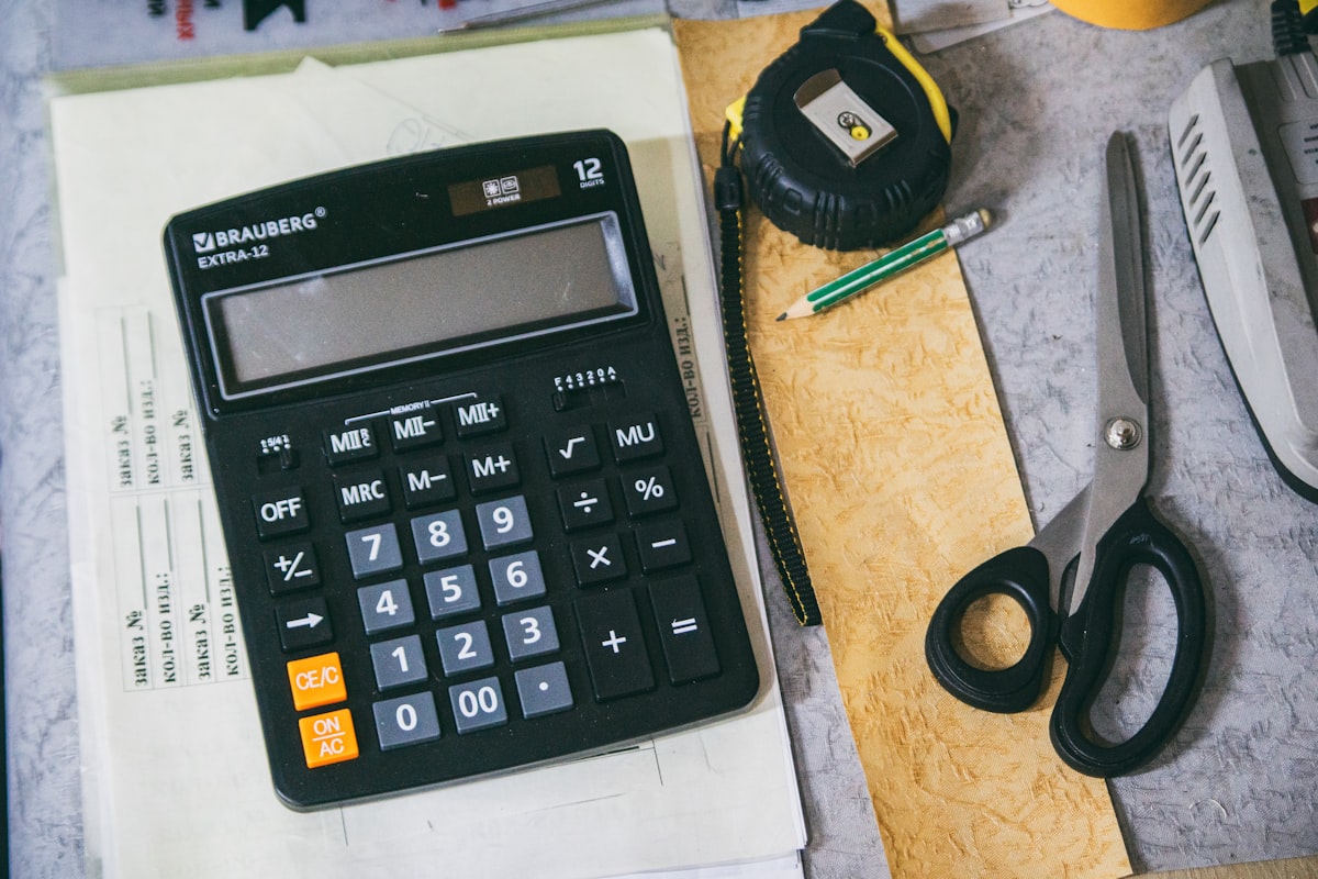 Hands typing an ingredient list into a laptop next to fresh produce and a calculator, using a nutrition calculator to work out recipe nutrition